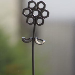 Op de afbeelding: Metalen bloemensculptuur. De bloemkop is gemaakt van zeven zeshoekige moeren, gerangschikt in een cirkel. De steel en bladeren zijn van metaal. Een uniek kunstwerk, geschikt voor interieurdecoratie.