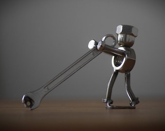 May include: A silver metal sculpture of a person made from nuts and bolts holding a wrench.