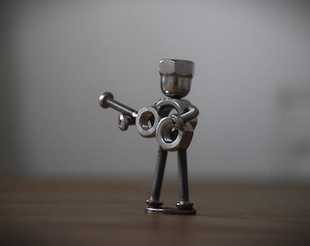 May include: A small metal figurine of a person playing a guitar made from nuts and bolts.