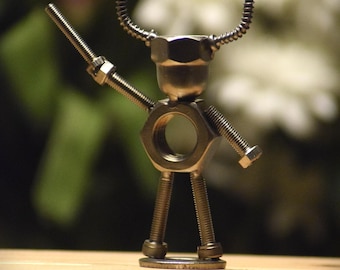 May include: A handcrafted metal sculpture of a figure, assembled from nuts, bolts, and screws. The figure has a head made from a hex nut, curved horns, and arms and legs made from bolts. The sculpture stands on a wooden surface.
