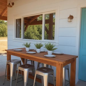May include: A wooden table with four metal bar stools sits on a patio. The table has a light brown wood finish and the stools are silver. There are plants in white pots on the table.