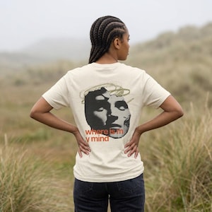 May include: A cream-colored short-sleeve t-shirt featuring a black and white graphic of a fragmented human face on the back. Above the face is a gold circular scribble design. The text "where is my mind" is printed in orange below the graphic.