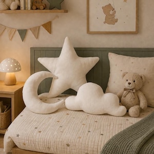 May include: A child's bedroom scene featuring a star, moon, and cloud-shaped cushions on a bed with a star-patterned quilt. A teddy bear and a framed bear picture are also visible. A mushroom lamp sits on a wooden bedside table.