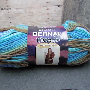 May include: A skein of Bernat Mosaic yarn, featuring a blend of blue, teal, and brown colors. The label indicates 100 g / 3.5 oz. The yarn is wrapped with a brown string. The label also includes a picture of a woman.