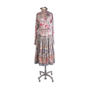 Peut inclure: Une robe vintage à imprimé floral avec un col montant à volants et des manches longues. La robe présente une jupe à volants et est présentée sur un mannequin roulant. Le tissu a un motif de fleurs roses, rouges et bleues.