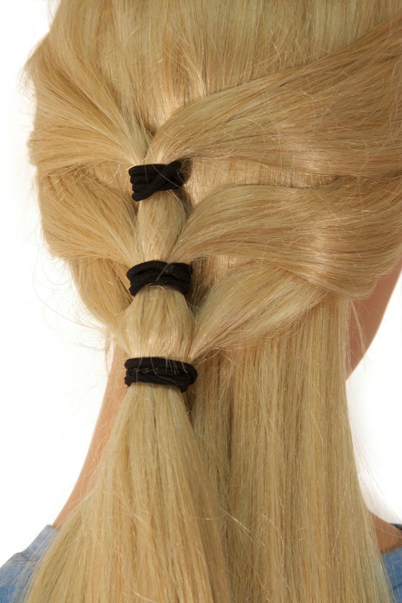 K&ouml;nnte beinhalten: Eine Frau mit langen, blonden Haaren, die zu einem Pferdeschwanz mit drei schwarzen Haargummis gebunden sind.