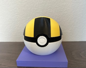 May include: A 3D printed Pokeball with black and yellow stripes and a white base. The Pokeball is sitting on a purple platform.