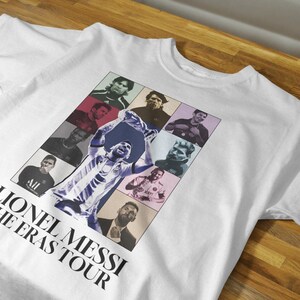 May include: White t-shirt featuring a collage of Lionel Messi images in various poses and eras. The shirt includes the text "Lionel Messi The Eras Tour" in a bold, black font, suitable for fans.
