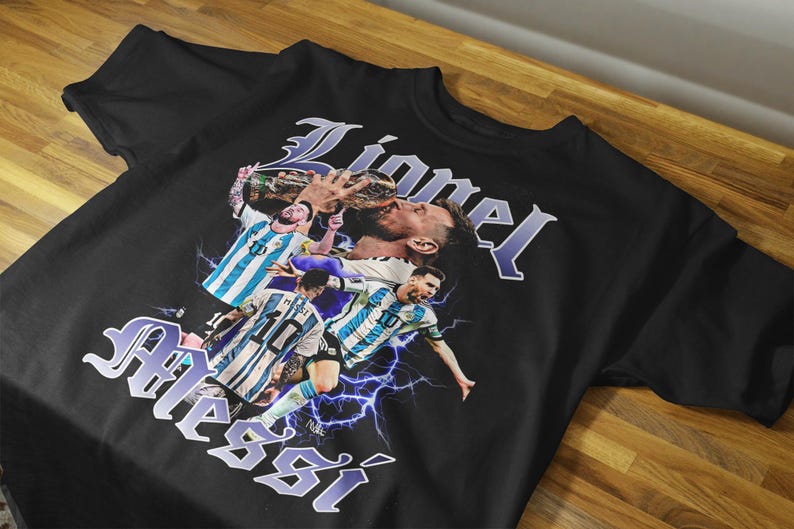 May include: Black t-shirt featuring a graphic of a soccer player with the name "Lionel Messi" in a stylized font. The design includes images of the player in action, with lightning bolt accents.