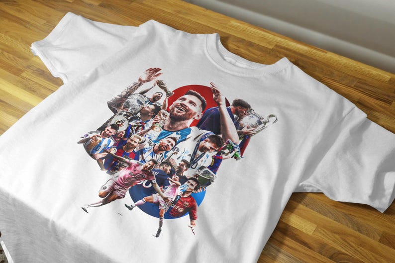 May include: White t-shirt featuring a collage of soccer players, including a central image of a smiling player. The design incorporates a red circle and a blue circle, with various action shots of players in different uniforms.