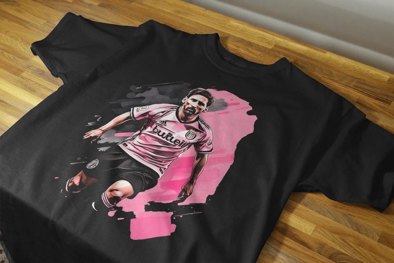 May include: Black t-shirt featuring a stylized illustration of a soccer player in a pink and white uniform. The graphic has a pink and black watercolor effect. The word "butleii" is visible on the shirt.