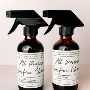 May include: Two brown glass spray bottles with black sprayers and white labels. The labels read "All Purpose Surface Clean" and "Thieves Natural Cleaning" with an 8 oz (236.58 ml) size.