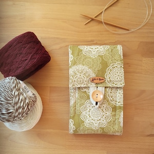 May include: A green fabric pouch with white lace patterns and a wooden button. The pouch has a label that says "Jute et Coton".