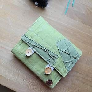 May include: A green quilted fabric notebook cover with two wooden buttons and a fabric flap. The cover has a patchwork design with a textured fabric.