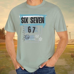 以下が含まれることがあります： 水色のTシャツ。黒い文字で「SIX SEVEN」と書かれた青い長方形のデザイン。その下に数字の「67」とスマイリーフェイスがあり、その下に「SIX SEVEN」と書かれています。柔らかい素材で作られたTシャツです。