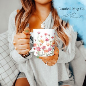 May include: White ceramic mug with a watercolor floral design featuring pink, yellow, and green flowers. The mug has a handle and the text "Nautical Mug Co." is visible in the background.