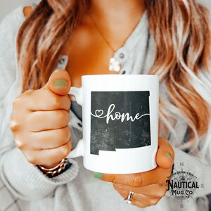 May include: White ceramic mug with a black outline of the state of New Mexico and the word "home" written in cursive with a heart above the "h".