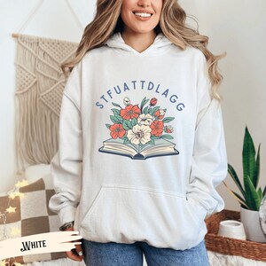 May include: White hooded sweatshirt with a graphic of a book with flowers and the text "STFUATTDLAGG" printed on the front.
