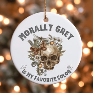 Puede incluir: Adorno de cer&aacute;mica blanca con una calavera rodeada de flores y una lib&eacute;lula. El texto "Morally Grey is my favorite color" est&aacute; impreso en el adorno.