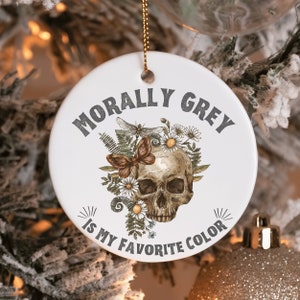 Puede incluir: Adorno de cer&aacute;mica blanca con una calavera rodeada de flores y una mariposa. El texto "Morally Grey is my favorite color" est&aacute; escrito alrededor de la calavera.