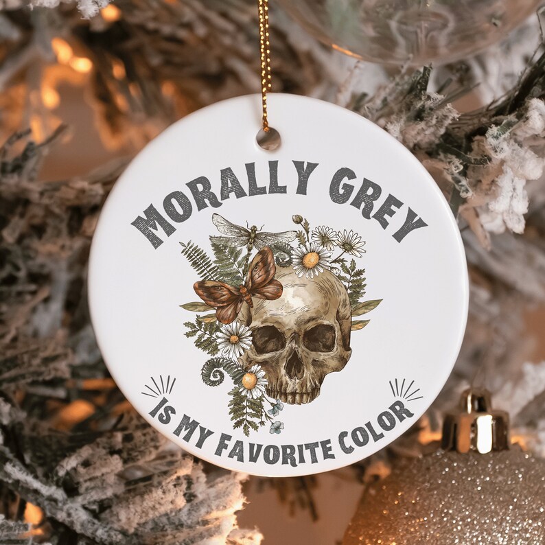 Puede incluir: Adorno de cer&aacute;mica blanca con una calavera rodeada de flores y una mariposa. El texto "Morally Grey is my favorite color" est&aacute; escrito alrededor de la calavera.