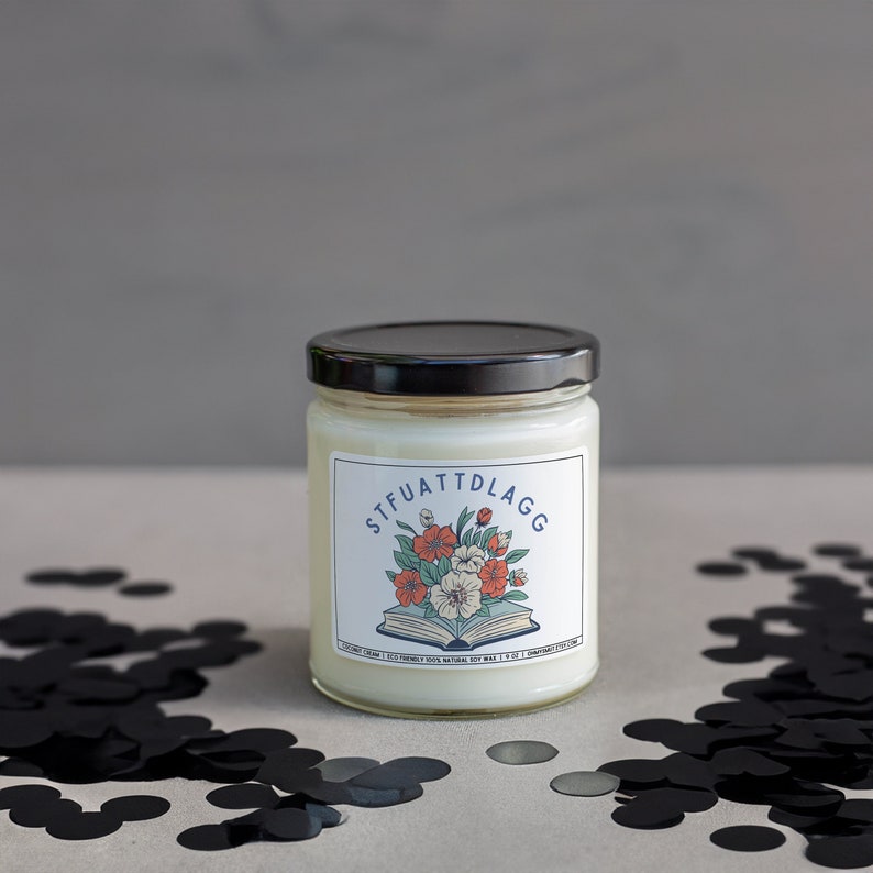 Może przedstawiać: Biały słoik ze świecą z czarną pokrywką i etykietą z napisem "STFUATTDLAGG". Etykieta przedstawia kwiatową ilustrację książki z kwiatami na g&oacute;rze. Słoik ze świecą stoi na powierzchni z czarnymi konfetti.