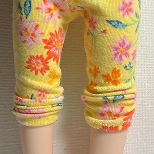 May include: Yellow leggings with a floral print featuring pink, orange, and white flowers. The leggings are made of a soft, stretchy fabric.