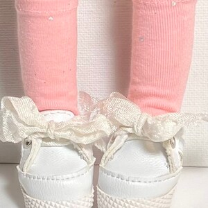 May include: A pair of white sneakers with white ribbon bows and pink socks with white polka dots.