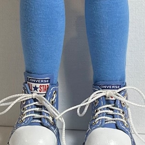 May include: A pair of blue knee-high socks with white Converse sneakers. The sneakers have blue laces and a white rubber sole. The text "Converse All Star" is visible on the sneakers.