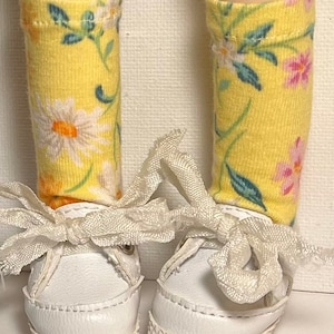May include: A pair of white canvas shoes with white laces tied in a bow. The shoes are worn with yellow socks with a floral pattern.