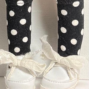 May include: A pair of white canvas shoes with white laces tied in a bow. The shoes are worn with black and white polka dot knee-high socks.