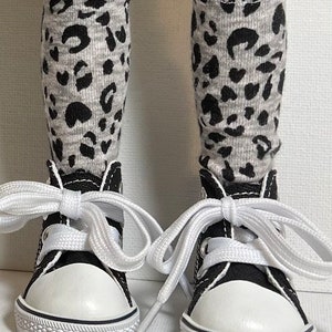 May include: A pair of black canvas high-top sneakers with white laces and white soles. The sneakers are worn with grey and black leopard print knee-high socks.
