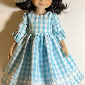 May include: A doll wearing a blue and white gingham dress with white embroidered trim and black shoes.