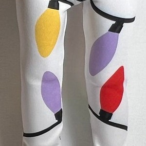 May include: White leggings with a colorful Christmas light pattern. The leggings have a black waistband and are made of a soft, stretchy fabric.