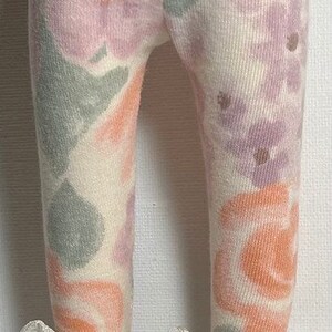May include: White leggings with a floral print in shades of pink, purple, and orange. The leggings are paired with white sneakers with white ribbon laces.