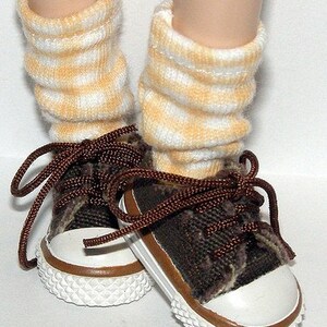 May include: A pair of brown canvas sneakers with white laces and white soles. The sneakers are worn with yellow and white striped socks.