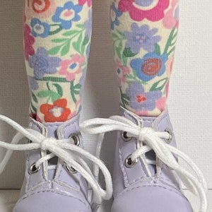 May include: A pair of lavender doll shoes with white laces and a floral print on the socks.