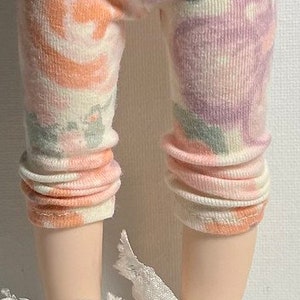 May include: White leggings with a floral pattern in shades of pink, orange, and green. The leggings are worn with white sneakers with white laces.
