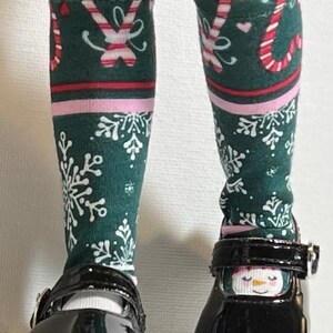May include: A pair of black patent leather shoes with a buckle closure. The shoes are worn with green and white striped knee-high socks featuring a candy cane and snowflake design.