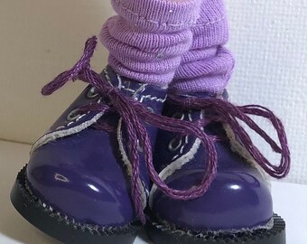 May include: A pair of purple leather shoes with white stitching and purple laces. The shoes have black soles and are worn with lavender socks.