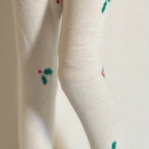 May include: White tights with a green and red holly pattern. The tights are worn by a doll with black patent leather shoes.