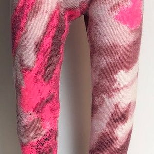 May include: A pair of brown and pink tie-dye leggings with a white background. The leggings are worn with brown leather mary jane shoes.