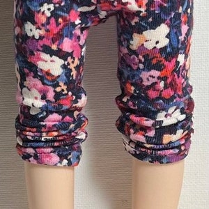 May include: Floral print leggings in shades of pink, purple, and white on a black background. The leggings are cropped and have a ribbed texture.