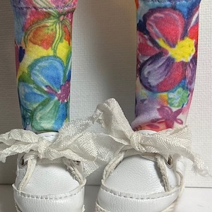 May include: A pair of white canvas shoes with white laces and a white ribbon tied around the ankles. The shoes are worn with colorful floral socks.
