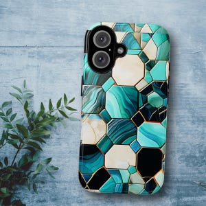 Puede incluir: Una funda para teléfono con un patrón geométrico en azul, blanco y negro. La funda tiene una protuberancia de cámara elevada con dos lentes.