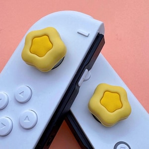 May include: Two white Nintendo Switch Joy-Con controllers with yellow star-shaped button covers.