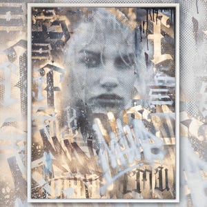 May include: A framed abstract art print with a black and white image of a face, layered over a gold and white background with black and white graffiti.