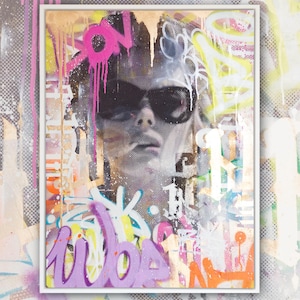 May include: A framed abstract painting with a person's face in the center. The face is partially obscured by sunglasses and graffiti-style text and designs in pink, purple, yellow, and orange.