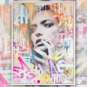 May include: A framed abstract painting with a woman's face in the center. The painting is done in a variety of colors, including pink, yellow, blue, and green. The woman's face is partially obscured by the colors, but her eyes and mouth are visible. The painting is surrounded by a white frame.