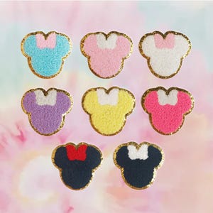May include: Eight embroidered iron-on patches in various colors, each featuring a cartoon mouse head with a bow. The patches are in the following colors: light blue, pink, white, purple, yellow, pink, black, and navy blue.